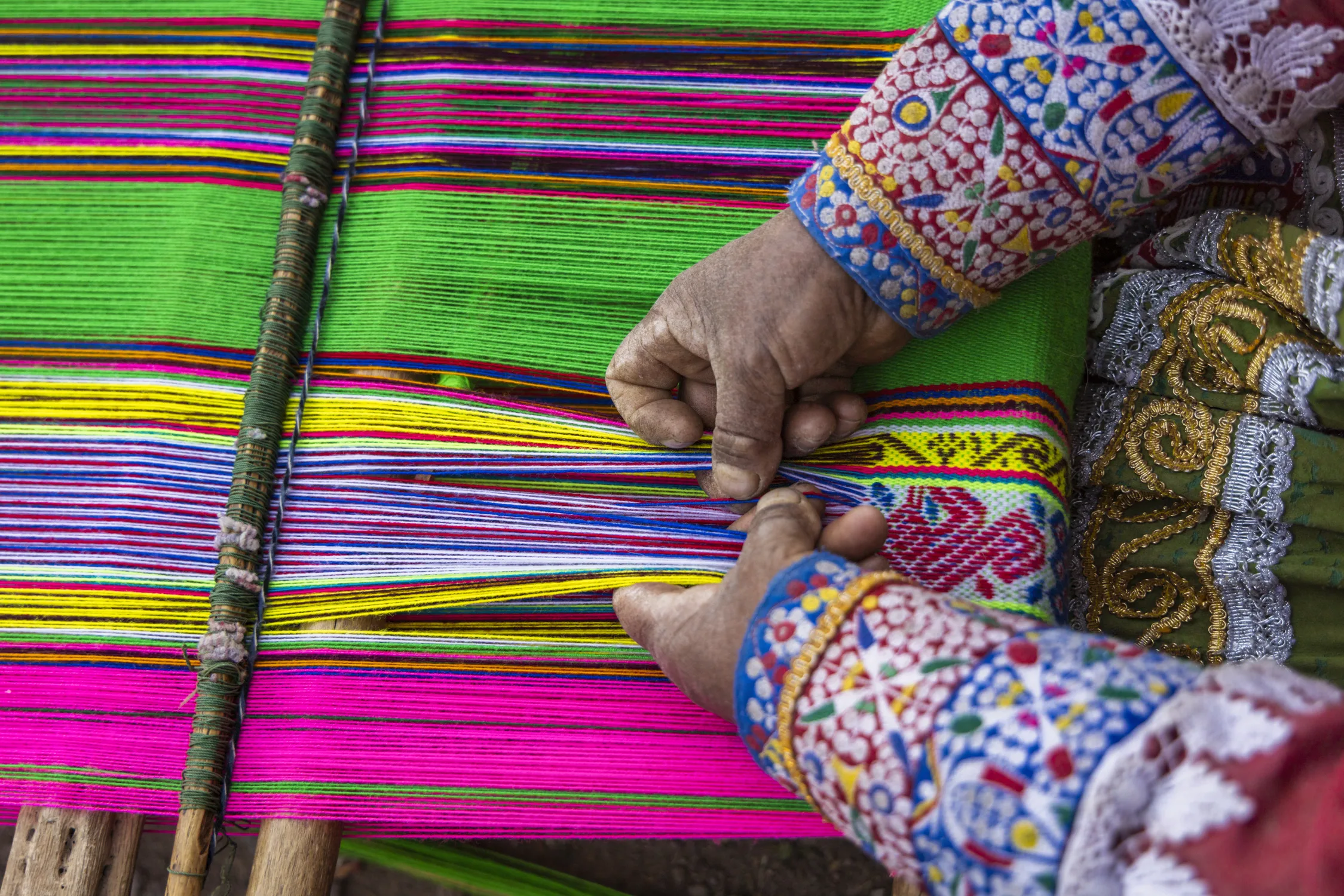 Hands weaving at a colorful loom
